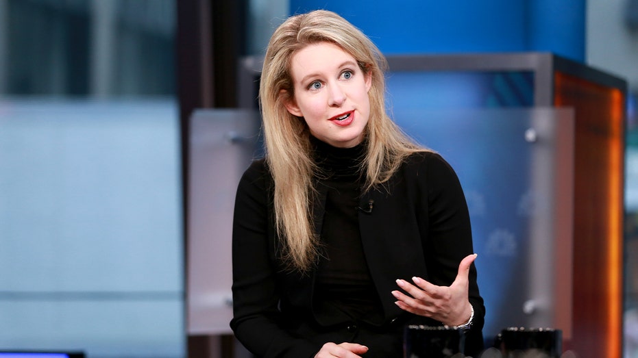 Elizabeth Holmes sits under studio lighting during a live business news broadcast.