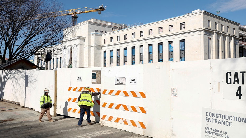 Construction worker walks past fencing into an active renovation area at a government building.