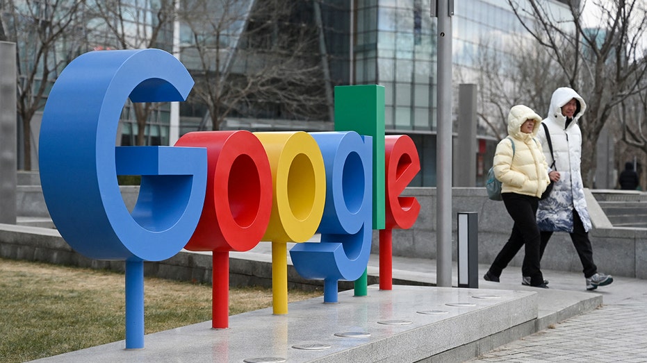 People walk by the Google logo sign outside of office