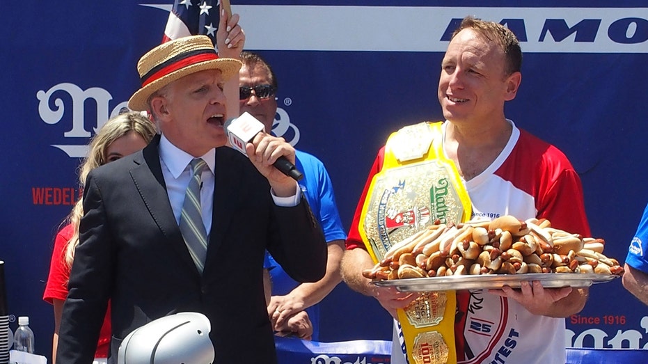 Joey Chestnut holds a plate of hot dogs and Mustard Belt