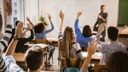 High school students raise their hands in a classroom.