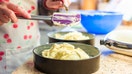 A senior woman bakes a cake in her kitchen at home. She is transferring the cake mixture into cake tins, before baking in the oven. Other ingredients are on the work surface, such as flour and vanilla essence. - Fox Business News