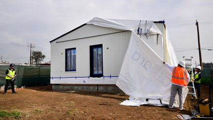 Workers remove the wrapping from the first free modular home for survivors of the 2025 Eaton Fire after it was set in place by a crane in Altadena, California, on January 22, 2025, more than a year after the fire destroyed some 9,400 structures. As part of its recovery efforts, the nonprofit coalition Steadfast LA has partnered with Samara, a modular house builder company, to provide homes at no cost to low-income Altadena and Pacific Palisades homeowners who lost their primary residences during the Eaton and Palisades wildfires of January 2025. - Fox Business News