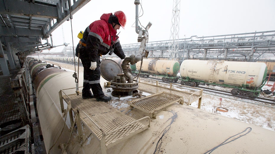 An industrial worker monitors fuel being pumped into rail tank cars at a large refinery complex.