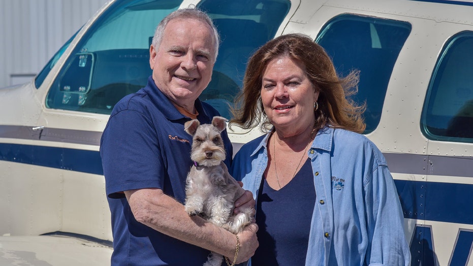 a couple holding a dog in front of plane