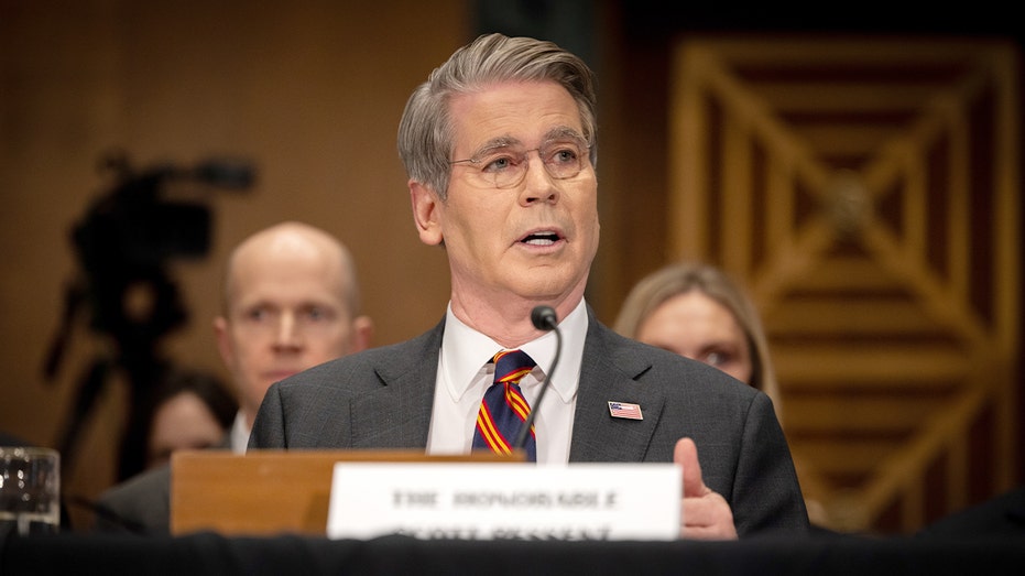 Scott Bessent sits at a hearing table, speaking into a microphone before lawmakers.