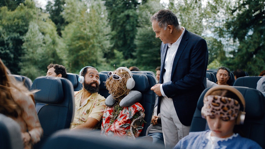 A man asking another man if he can sit in the chair next to him