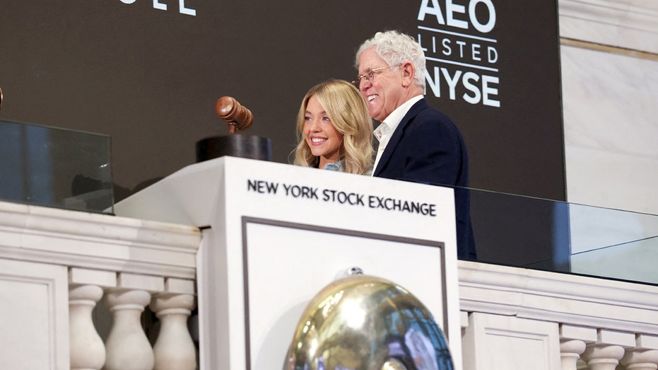 Sydney Sweeney poses with a retail executive on the NYSE trading floor following a ceremonial market opening.