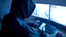 A hacker sits behind computer monitors and uses a mobile phone. - Fox Business News