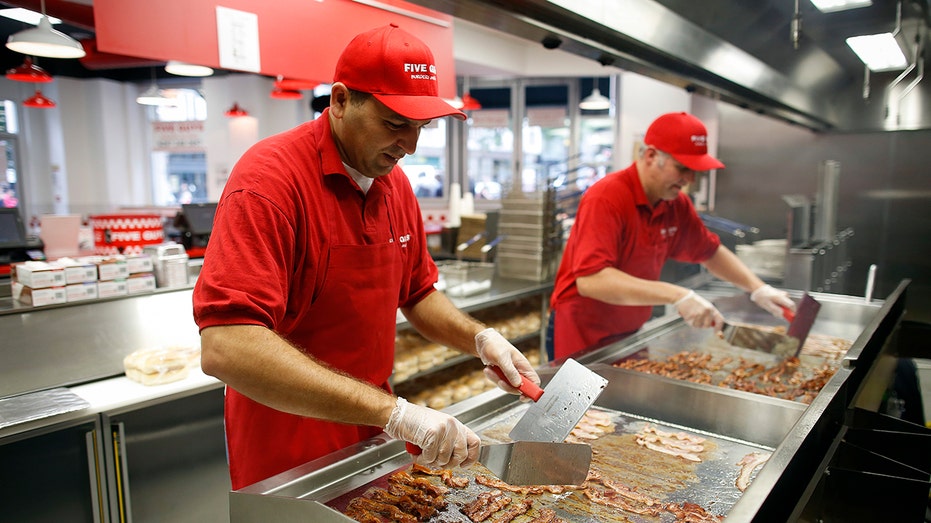 Chefs fry bacon on a griddle in the kitchen at U.S. burger restaurant chain Five Guys