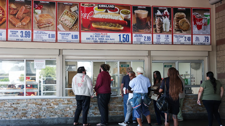 Customers wait in line to order below signage for the Costco Kirkland Signature $1.50 hot dog