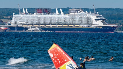 The cruise ship "Disney Adventure", built in the Wismar shipyard, is moored in the port of Mukran on the island of R&uuml;gen, while bathers and a windsurfer are in the water in the foreground. After around seven years of construction, one of the world's largest cruise ships starts its test voyages. The US shipping company Disney Cruise Line took over the ship from the insolvency estate and is having it built by the Meyer shipyard in Papenburg, Lower Saxony. The ship will be in service for the Disney Group in Southeast Asia from the end of 2025. - Fox Business News