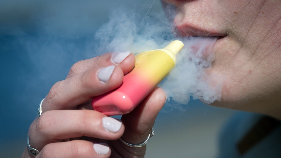 A woman poses for a photograph holding a single-use vape