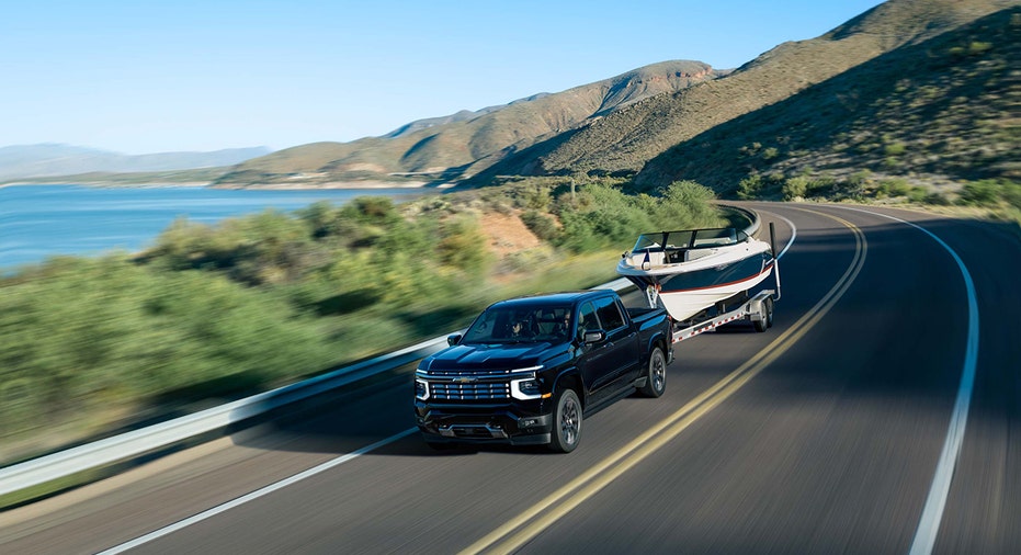 A 2027 Chevrolet Silverado 1500 High Country in Black tows a boat along a mountain road.