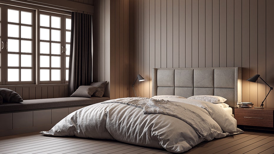 A dark brown bedroom with vertical wall paneling features a gray upholstered bed, built-in window seat and bedside lamps. Zillow said chocolate brown bedrooms can add an estimated $2,277 to a home’s offer price.
