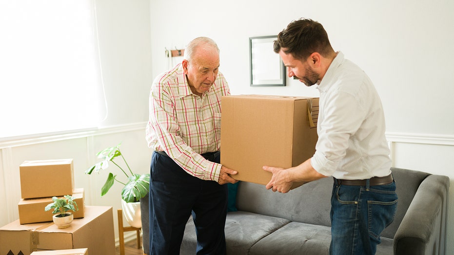 A father helps his adult son move boxes, reflecting a growing trend of young adults delaying independent living amid elevated housing costs.