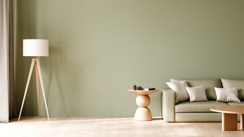 A sage green living room features a matching sofa, wooden accent tables and a tripod floor lamp. Zillow said sage green was one of the safest paint choices for sellers.