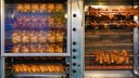Rotisserie chickens roasting on spits inside a commercial oven at a grocery store deli.
