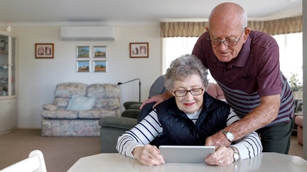An older couple sits at a table in their house looking at an electronic device. - Fox Business News