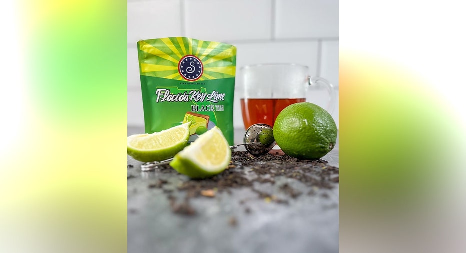 A green package of Star Spangled Florida Key Lime black tea displayed with a glass of tea, loose tea leaves and fresh lime wedges.