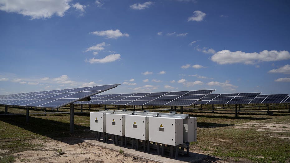 Power inverters sit beside solar panels at a utility-scale solar energy facility