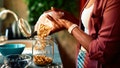 Close-up of a woman's hands pouring granola from a paper bag into a glass jar, with a bowl of blueberries in the foreground, suggesting a healthy breakfast preparation - Fox News