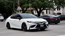  A portrait of a white Toyota Camry sedan traveling down a highway in moderate traffic. - Fox Business News