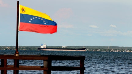 A Venezuelan flag waves in front of oil tanker on lake in Maracaibo, Venezuela on July 27, 2026. The capital of the oil state and surrounding areas offer a stark contrast between Venezuela's oil wealth and the daily reality of communities living near the country's energy infrastructure. While oil continues to generate revenue and crude is shipped through terminals serving international markets, many local residents say they have seen little benefit from the sector. - Fox Business News
