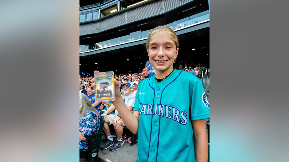 Thirteen-year-old Mariners fan Abby holds the one-of-one gold Jimothy rookie card at T-Mobile Park