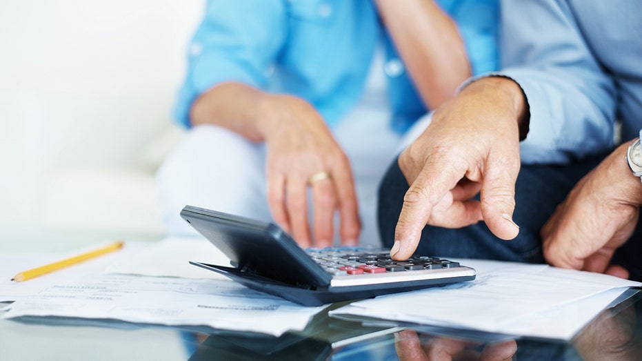 A couple reviews financial documents and uses a calculator while planning their finances.