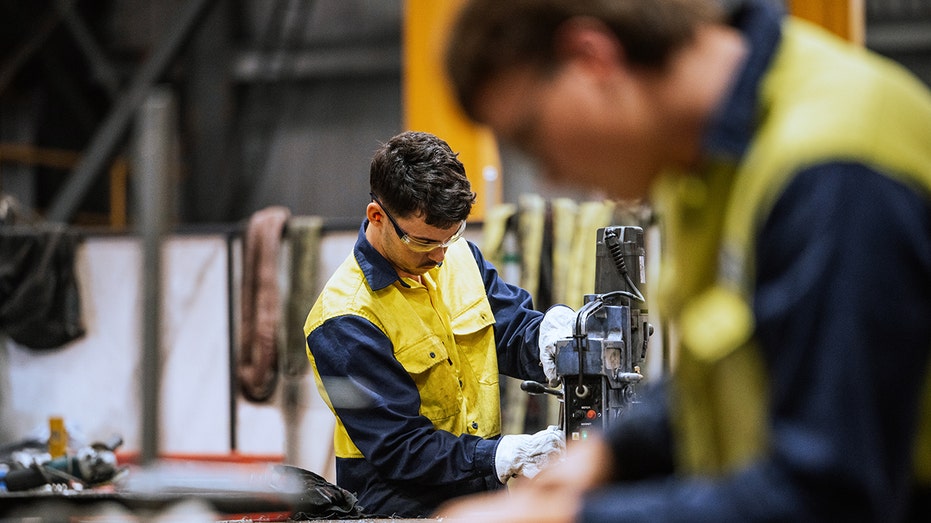Qualified welders working on steel construction, grinding and welding iron parts in modern bright warehouse