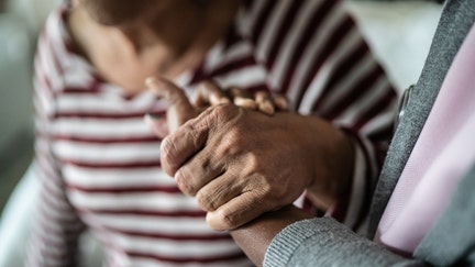 Nurse or home caregiver and senior woman holding hands at home - Fox Business News