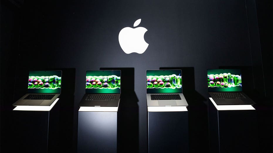 Four Apple MacBook Pro laptops displayed on illuminated stands beneath a large Apple logo