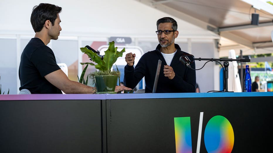Google CEO Sundar Pichai gestures while speaking with another person at a Google I/O event