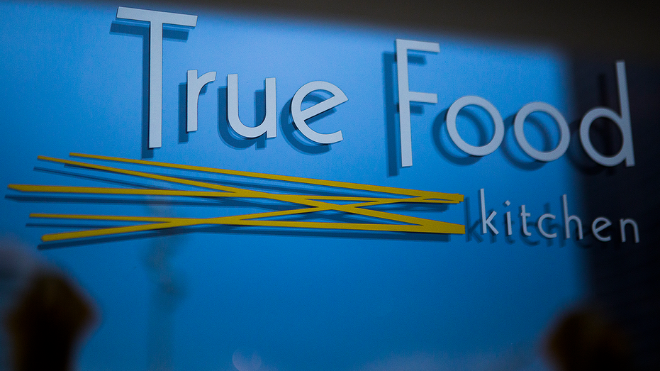 True Food Kitchen logo with white lettering and a yellow design on a blue wall