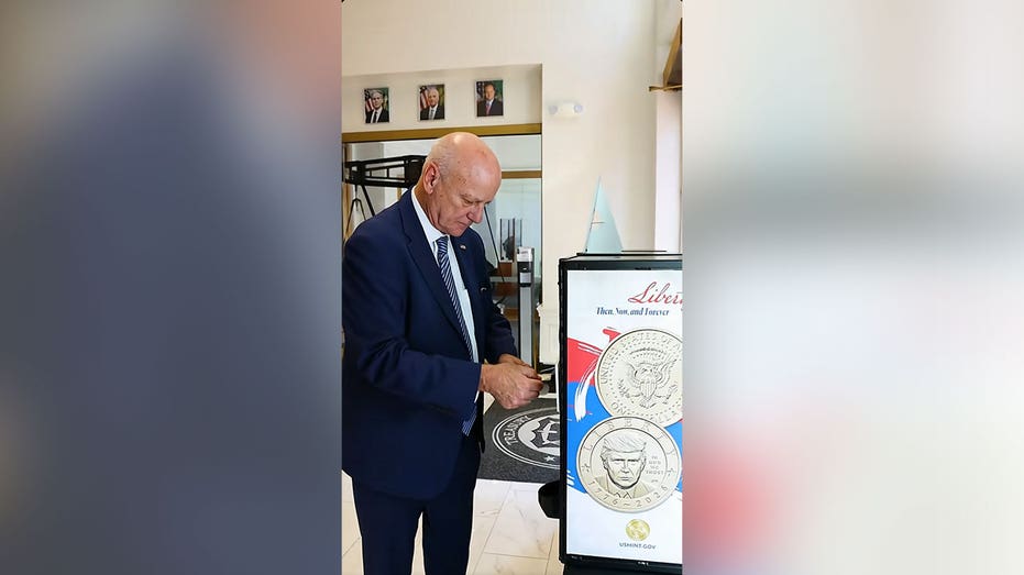 U.S. Treasurer Brandon Beach stands next to a display showing the new Trump dollar coin.