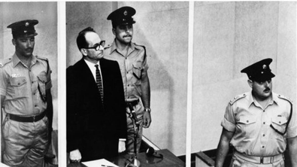 1962: Adolf Eichmann stands in his glass cage, flanked by guards, in the Jerusalem courtroom where he was tried for war crimes committed during World War II. The basics of Adolf Eichmann's story are well-documented. He was commonly known as the 