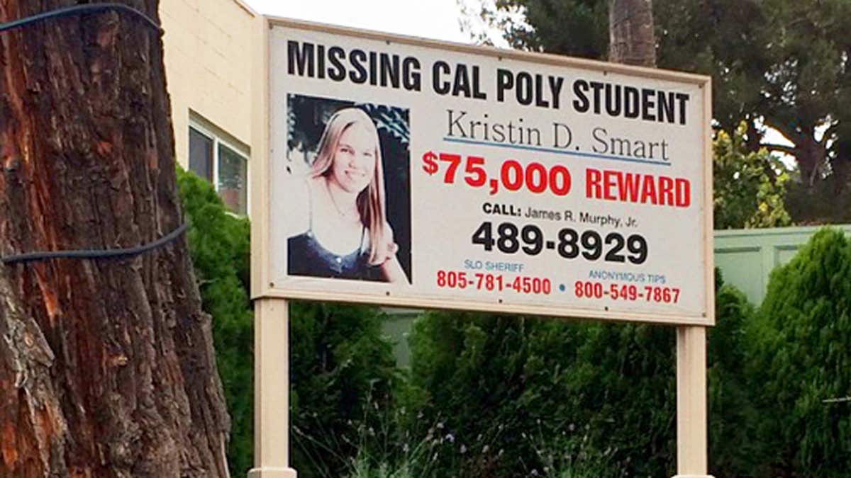 A billboard displaying missing person Kristin Smart near a tree and houses
