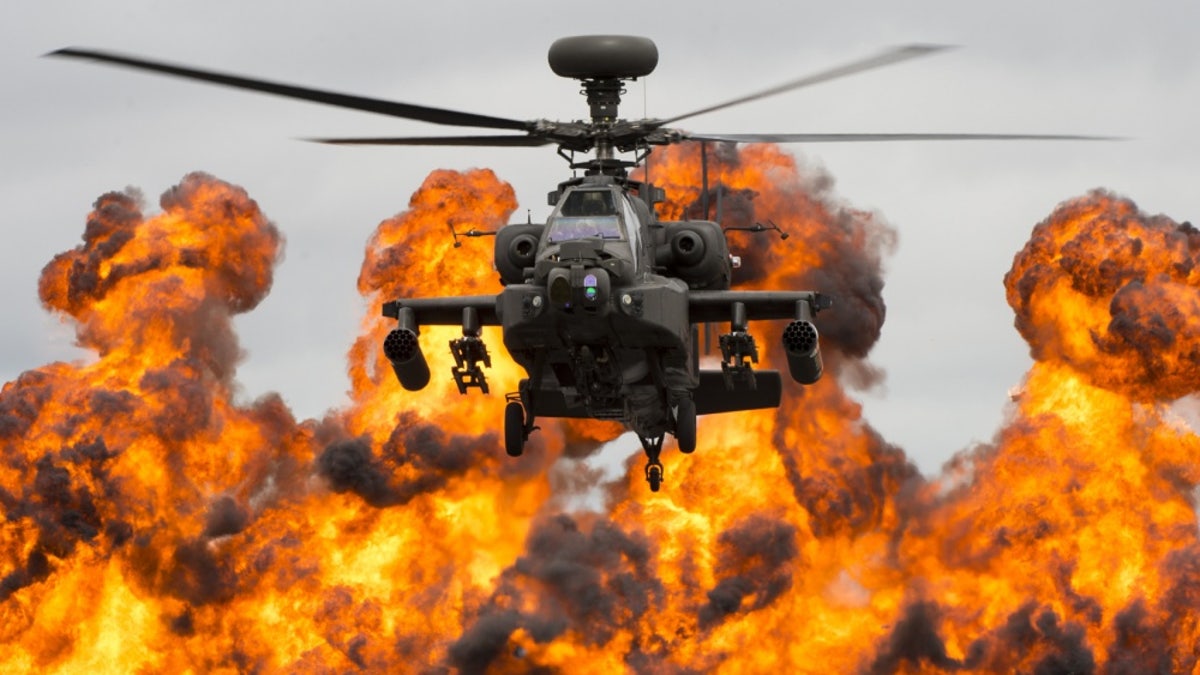 A Boeing Apache attack helicopter flies away from an explosion.