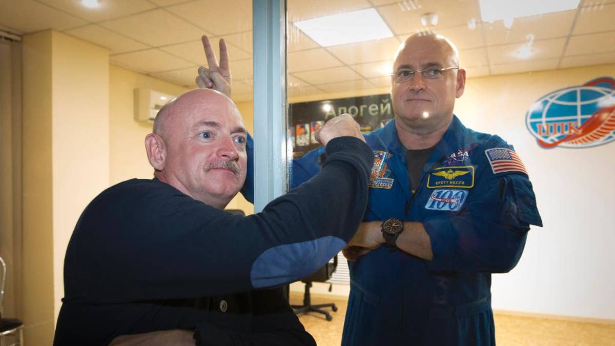 U.S. astronaut Scott Kelly, right, crew member of the mission to the International Space Station, ISS, poses through a safety glass with his brother, Mark Kelly, also an astronaut after a news conference in Russian leased Baikonur cosmodrome, Kazakhstan, Thursday, March 26, 2015.  Start of the new Soyuz mission is scheduled on Saturday, March 28.(AP Photo/Dmitry Lovetsky)