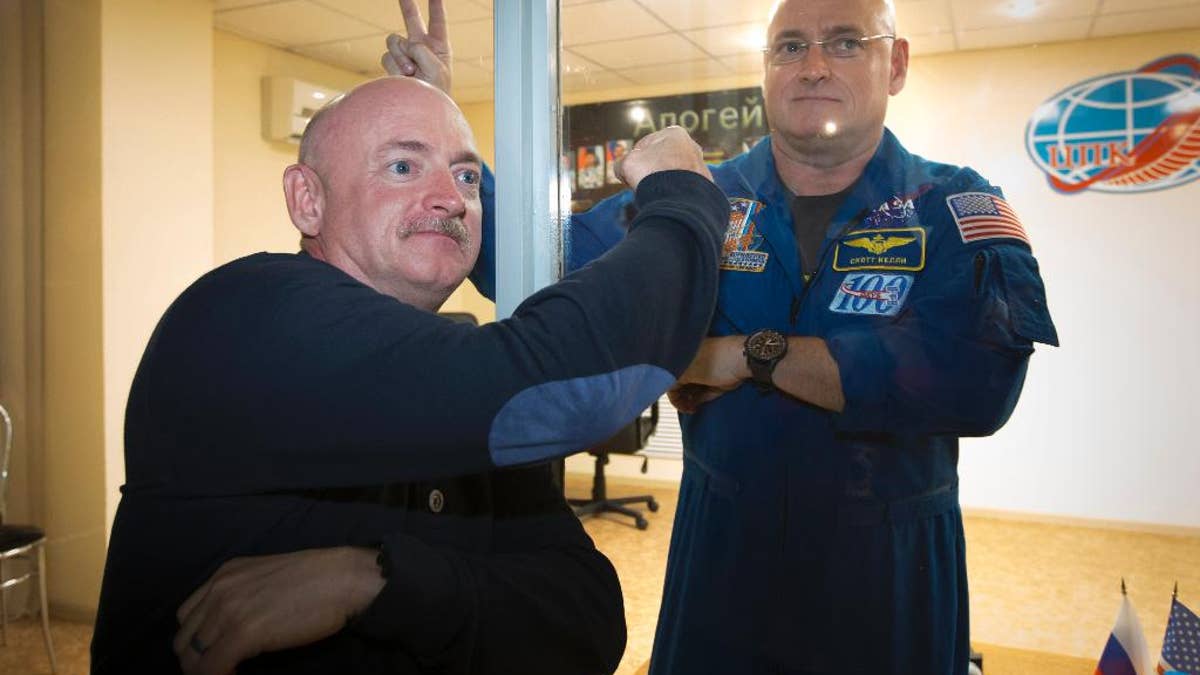 U.S. astronaut Scott Kelly, right, crew member of the mission to the International Space Station, ISS, poses through a safety glass with his brother, Mark Kelly, also an astronaut after a news conference in Russian leased Baikonur cosmodrome, Kazakhstan, Thursday, March 26, 2015.  Start of the new Soyuz mission is scheduled on Saturday, March 28.(AP Photo/Dmitry Lovetsky)