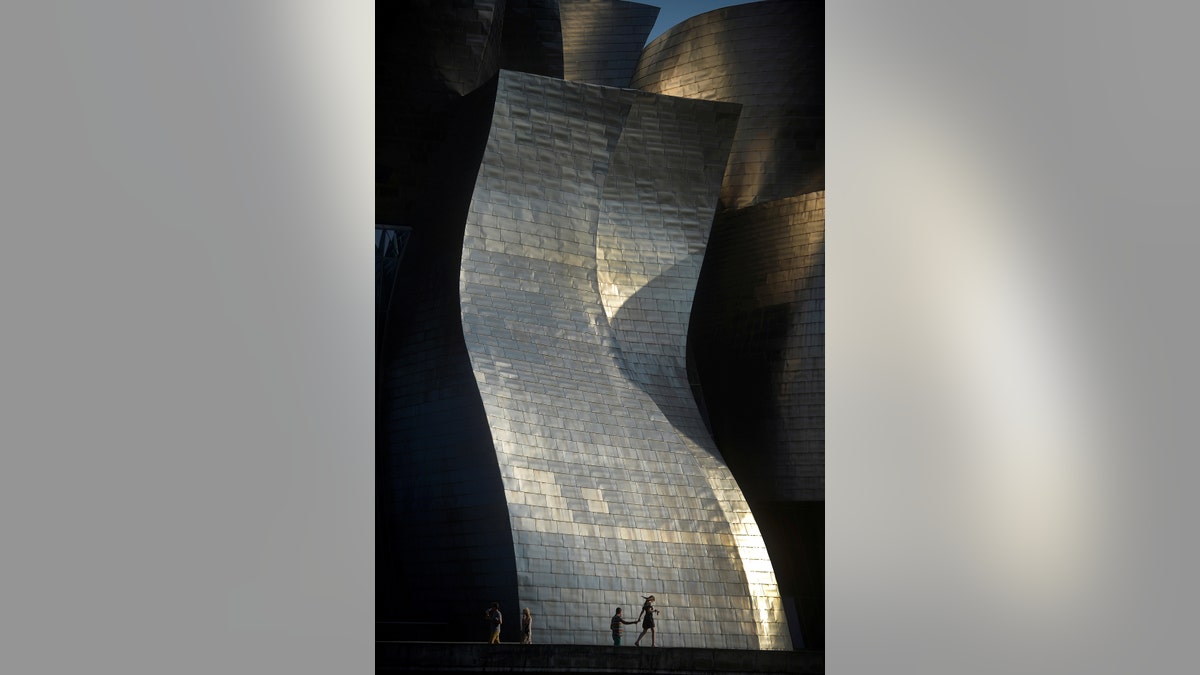 A couple walks past the Guggenheim Museum illuminated by the late afternoon sun in Bilbao, Spain, July 17, 2017. REUTERS/Vincent West     TPX IMAGES OF THE DAY - RTX3BUI8
