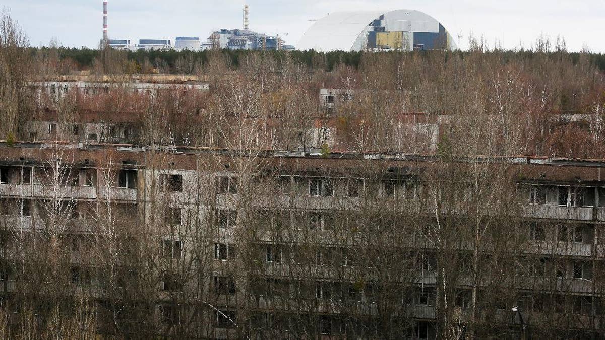 This photo taken Wednesday, March 23, 2016 shows abandoned apartment buildings  in the town of Pripyat near Chernobyl, Ukraine, with a chimney, left, at the destroyed reactor and a gigantic  arch-shape confinement to cover the remnants of the exploded reactor, in the back, at the Chernobyl nuclear power plant. Thirty years after the world’s worst nuclear accident, the Chernobyl nuclear power plant is surrounded by both a hushed desolation and clangorous activity, the sense of a ruined past and a difficult future. (AP Photo/Efrem Lukatsky)