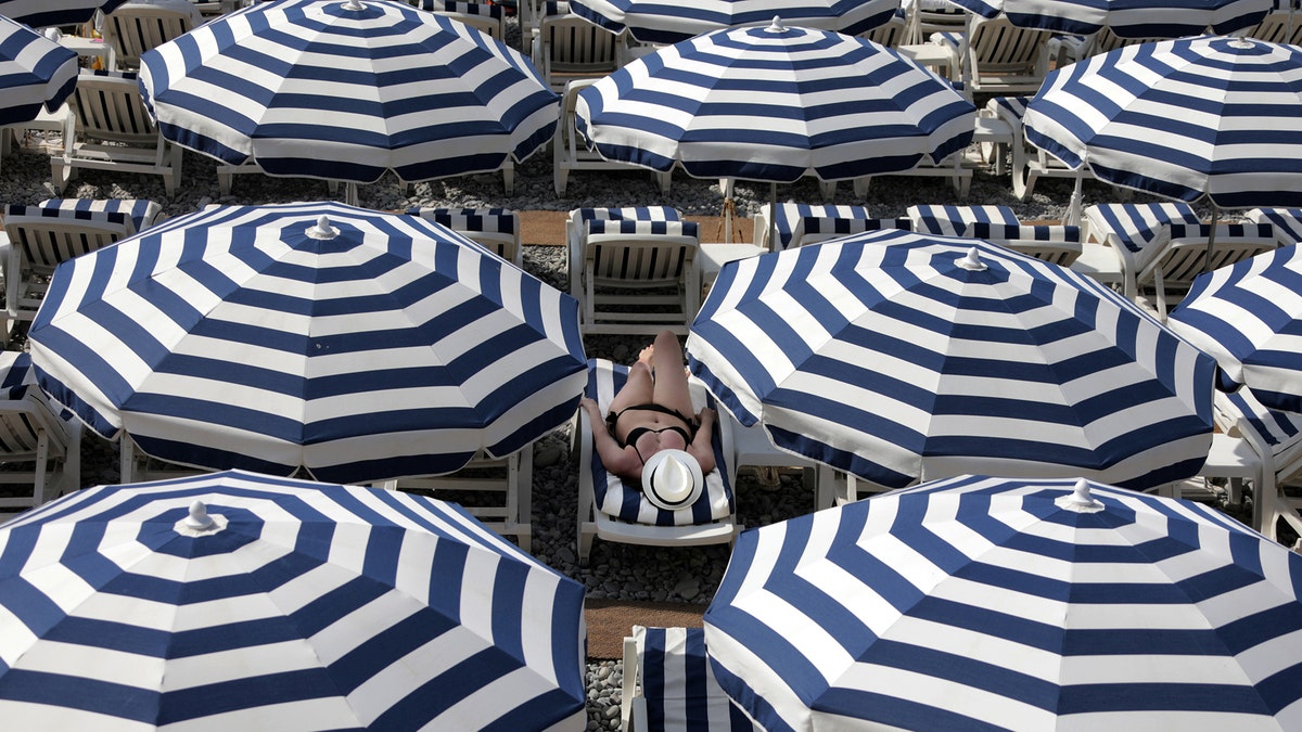 A tourist enjoys the sun on a beach covered with umbrellas on the Promenade Des Anglais during a sunny summer day in Nice, France, July 11, 2017. REUTERS/Eric Gaillard TPX IMAGES OF THE DAY - RTX3AZZ1