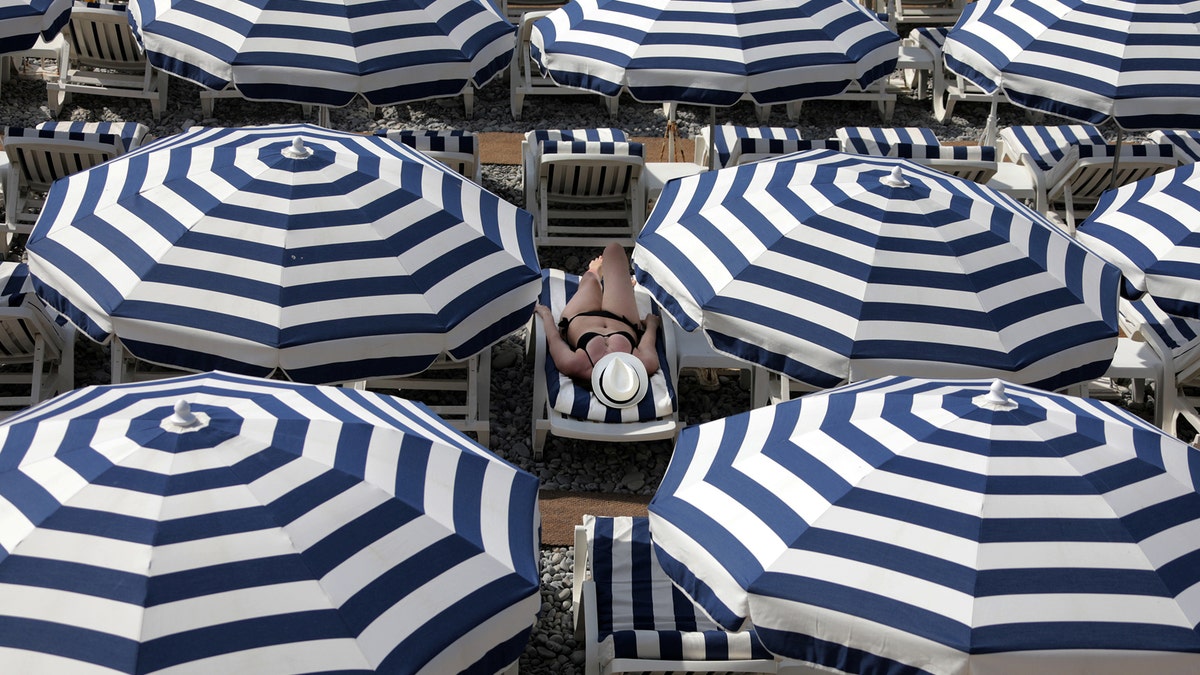 A tourist enjoys the sun on a beach covered with umbrellas on the Promenade Des Anglais during a sunny summer day in Nice, France, July 11, 2017. REUTERS/Eric Gaillard TPX IMAGES OF THE DAY - RTX3AZZ1