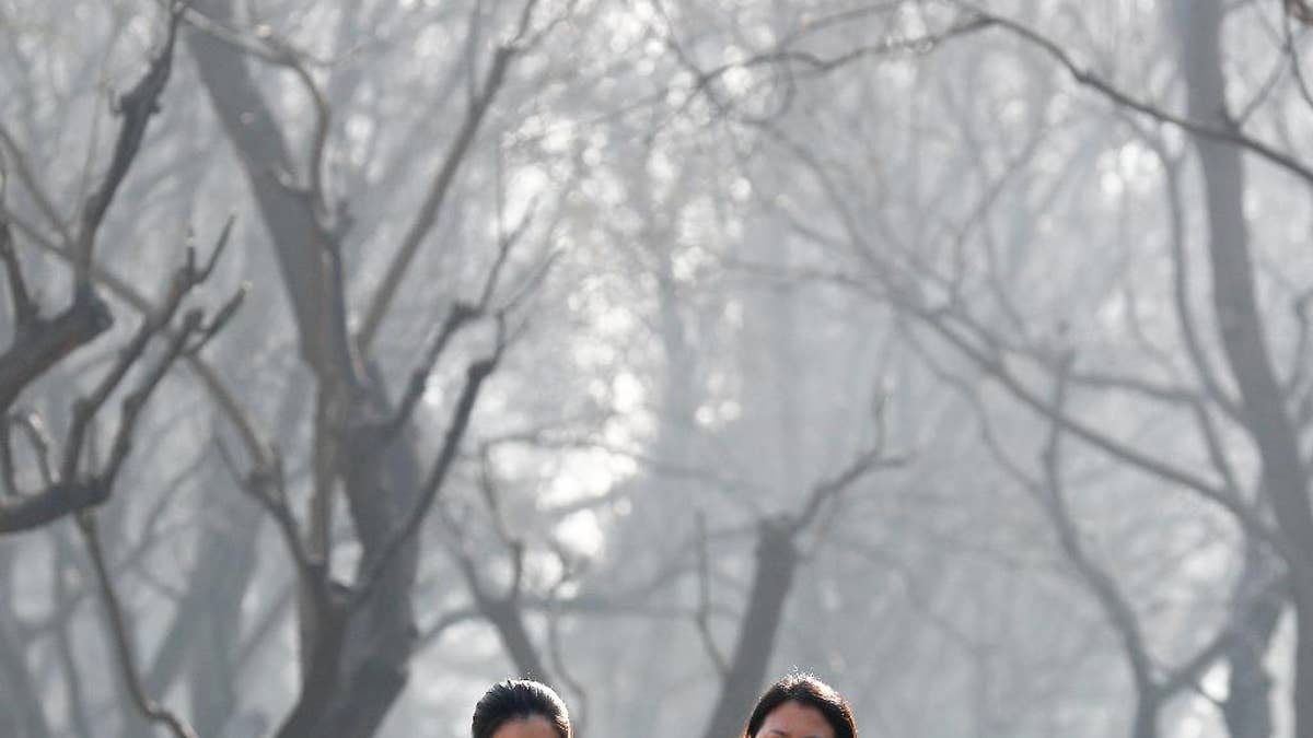 FILE - In this Dec. 19, 2016, file photo, Chinese women wearing masks to protect themselves from air pollution walk through Ritan Park shrouded by dense smog in Beijing. China's government said on Wednesday, March 29, 2017, it will stick to its promises to curb carbon emissions after President Donald Trump eased U.S. rules on fossil fuel use that were meant to control global warming. A Chinese foreign ministry spokesman said Beijing is committed to the Paris climate agreement. (AP Photo/Andy Wong, File)