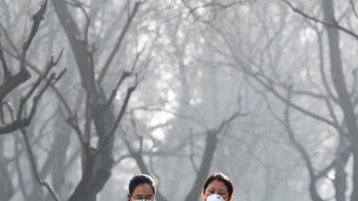 FILE - In this Dec. 19, 2016, file photo, Chinese women wearing masks to protect themselves from air pollution walk through Ritan Park shrouded by dense smog in Beijing. China's government said on Wednesday, March 29, 2017, it will stick to its promises to curb carbon emissions after President Donald Trump eased U.S. rules on fossil fuel use that were meant to control global warming. A Chinese foreign ministry spokesman said Beijing is committed to the Paris climate agreement. (AP Photo/Andy Wong, File)