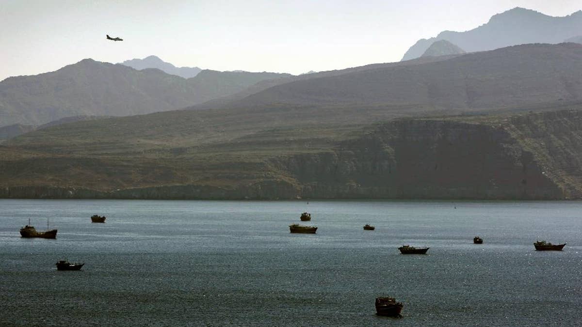 FILE - In this Jan. 19, 2012 file photo, a plane flies over the mountains in south of the Strait of Hormuz as the trading dhows and ships are docked on the Persian Gulf waters near the town of Khasab, in Oman. The operator of a Marshall Islands-flagged cargo vessel boarded by Iranian forces as it was traversing the Strait of Hormuz said Wednesday, April 29, 2015 that it has confirmed the crew is safe but that the company is still trying to determine why the ship was seized the previous day by the Islamic Republic. (AP Photo/Kamran Jebreili, File)