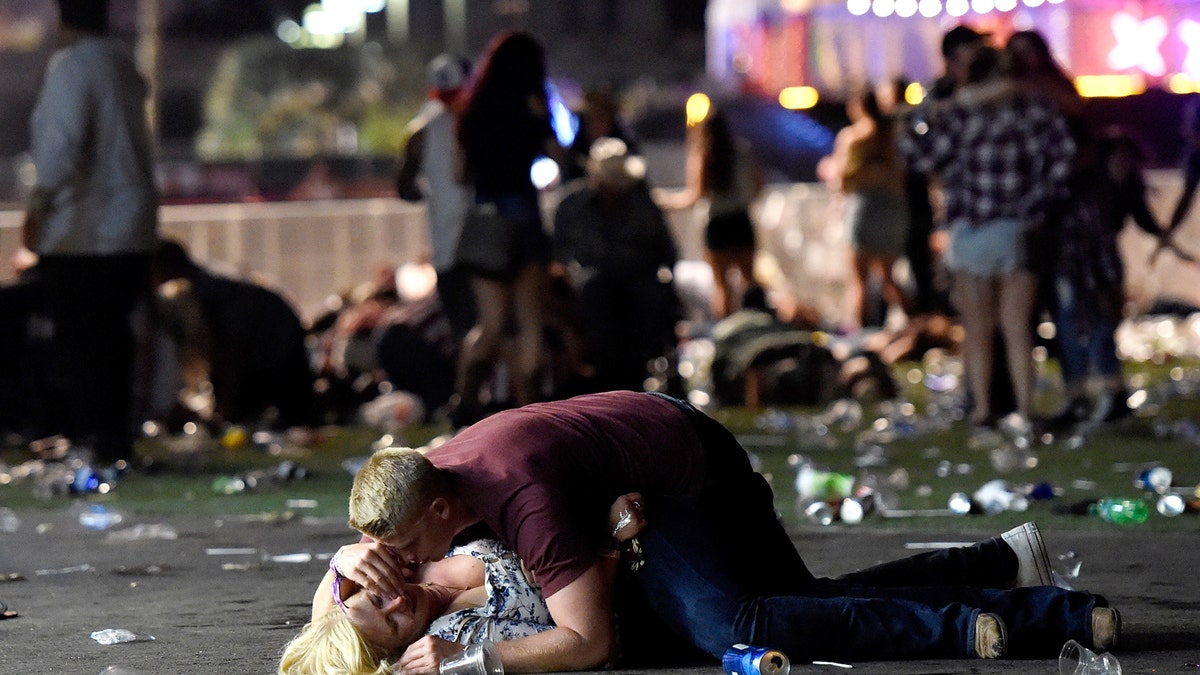 LAS VEGAS, NV - OCTOBER 01:  A man lays on top of a woman as others flee the Route 91 Harvest country music festival grounds after a active shooter was reported on October 1, 2017 in Las Vegas, Nevada. A gunman has opened fire on a music festival in Las Vegas, leaving at least 2 people dead. Police have confirmed that one suspect has been shot. The investigation is ongoing. (Photo by David Becker/Getty Images)