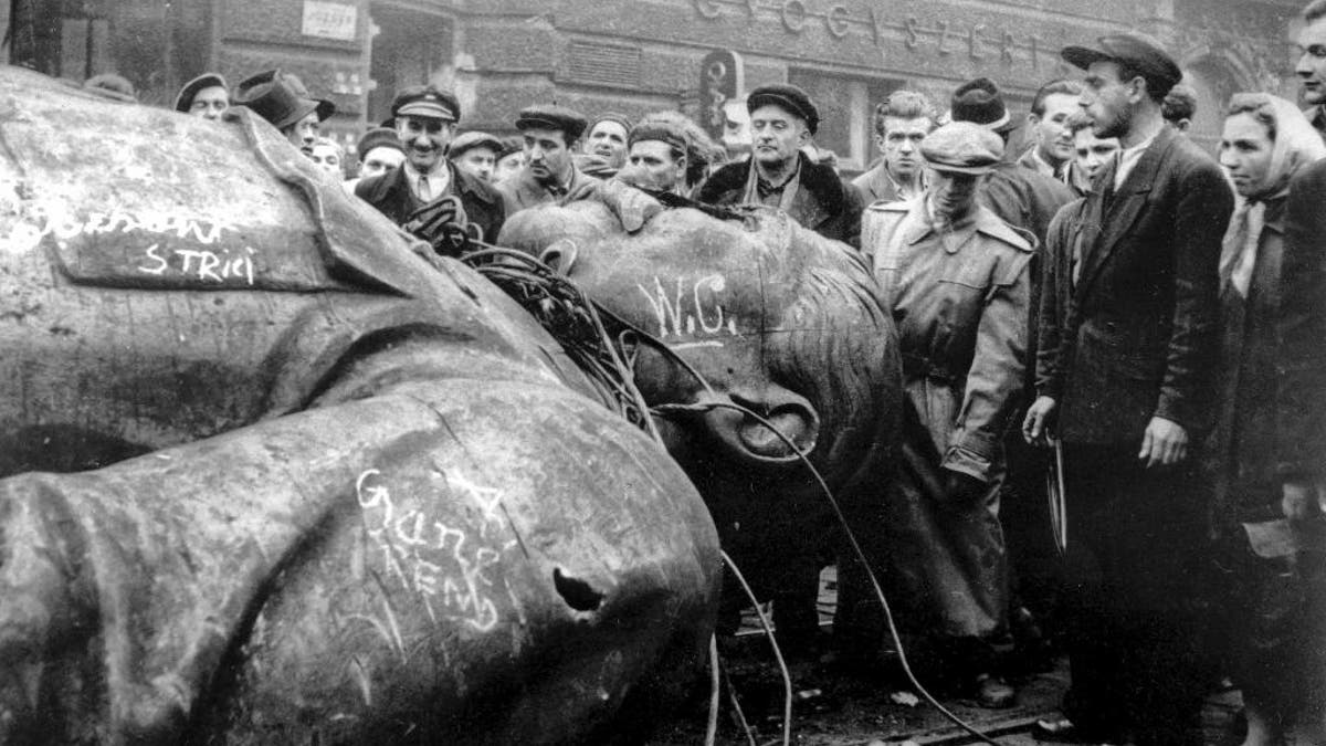 FILE - In this Oct. 24, 1956 file photo, people gather around a fallen statue of Soviet leader Josef Stalin in front of the National Theater in Budapest, Hungary. The uprising in Hungary began on Oct. 23, 1956 with demonstrations against the Stalinist regime in Budapest and was crushed eleven days later by Soviet tanks amid bitter fighting. For Hungary, a pro-Russian leader in the White House offers hope the Western world might end the sanctions imposed over Russia’s annexation of Crimea and its role in eastern Ukraine. Many Poles, instead, fear a U.S-Russian rapprochement under Trump could threaten their own security interests. To most Poles, NATO represents the best guarantee for an enduring independent state in a difficult geographical neighborhood. (AP Photo/Arpad Hazafi, file)